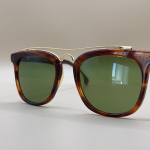 May include: Brown tortoiseshell sunglasses with green lenses. The sunglasses have a gold-colored metal bridge and arms. The frames are a classic shape, suitable for various face shapes. The lenses are a solid green color.