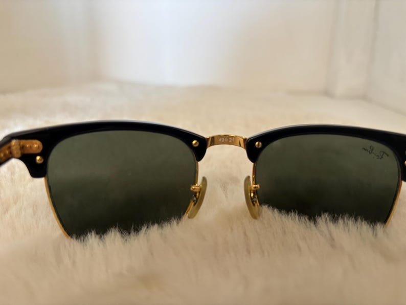 May include: Black and gold sunglasses with green lenses. The sunglasses feature a classic design with a black upper frame and gold accents. The lenses are a dark green colour, and the frame has a gold bridge and hinges.