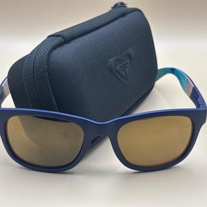 May include: Navy blue sunglasses with brown lenses and a matching case. The sunglasses have a square frame and patterned arms. The case has a zip and a logo.