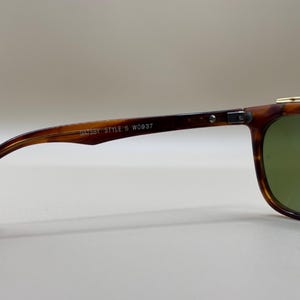 May include: Close-up of vintage sunglasses with a tortoiseshell frame and green lenses. The arm of the glasses has the text "GATSBY STYLE 5 W0937". The glasses have a gold-colored top bar.