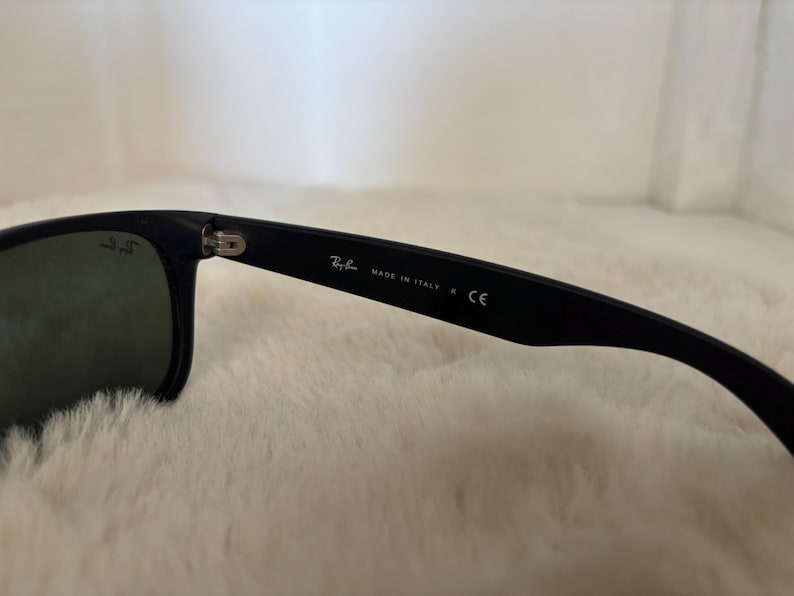 K&ouml;nnte beinhalten: Schwarze Sonnenbrille mit dunklen Gl&auml;sern. Der Rahmen ist schwarz mit dem Text "MADE IN ITALY" und dem Ray-Ban-Logo auf dem B&uuml;gel. Die Gl&auml;ser sind dunkelgr&uuml;n.