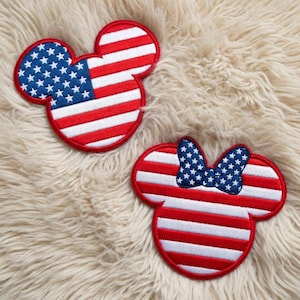 May include: Two embroidered patches in the shape of Mickey Mouse heads, featuring the American flag design. One patch has the stars and stripes, while the other has a bow with stars. The patches are red, white, and blue, with a red border.