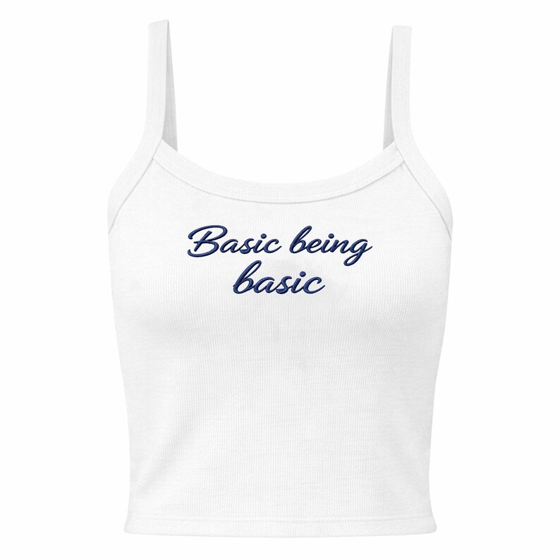May include: White ribbed vest top with thin straps. The text "Basic being basic" is printed in a dark blue script across the front. The top is a casual style, suitable for layering or warm weather.