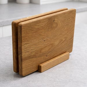 Könnte beinhalten: Ein Holzschneidebrett-Set mit natürlicher Holzmaserung. Das Set enthält zwei rechteckige Bretter und einen kleinen rechteckigen Ständer. Die Bretter sind etwa 30 cm lang und 23 cm breit.