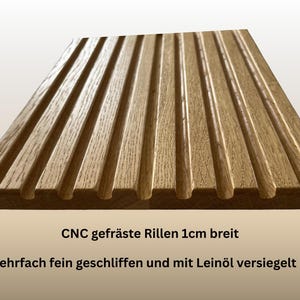 May include: A rectangular wooden board with parallel grooves, likely for a kitchen or decorative purpose. The wood has a warm, natural tone. The text on the board reads "CNC milled grooves 1cm wide" and "Multiple finely ground and sealed with linseed oil."