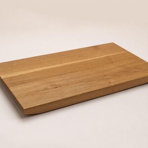 May include: A rectangular wooden cutting board with a natural light brown grain pattern. The board features a smooth, flat top surface and slightly beveled edges, showcasing the organic texture and warm tones of the wood material throughout.