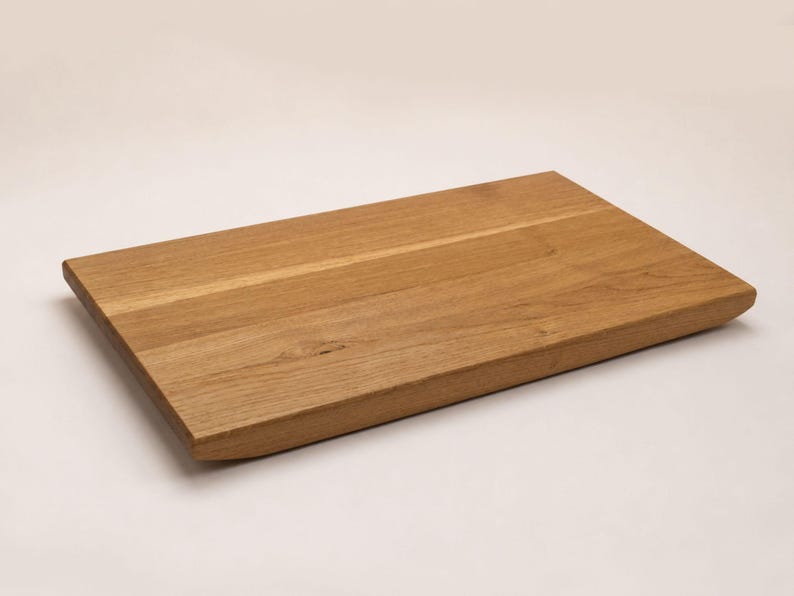 May include: A rectangular wooden cutting board with a natural light brown grain pattern. The board features a smooth, flat top surface and slightly beveled edges, showcasing the organic texture and warm tones of the wood material throughout.
