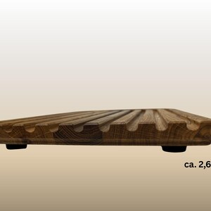 May include: A wooden breadboard with a grooved surface and rounded edges. The board is approximately 1 inch thick and rests on two small black feet. The wood has a warm, natural tone.