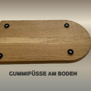 May include: A light brown wooden cutting board with a rounded edge and four black rubber feet. The text "Gummif&uuml;&szlig;e am Boden" is printed in black at the bottom of the image.