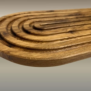 May include: A wooden breadboard with a unique design. The board is made of light brown wood and features a series of concentric, curved grooves. The grooves create a visually appealing texture and are ideal for serving bread or other foods.