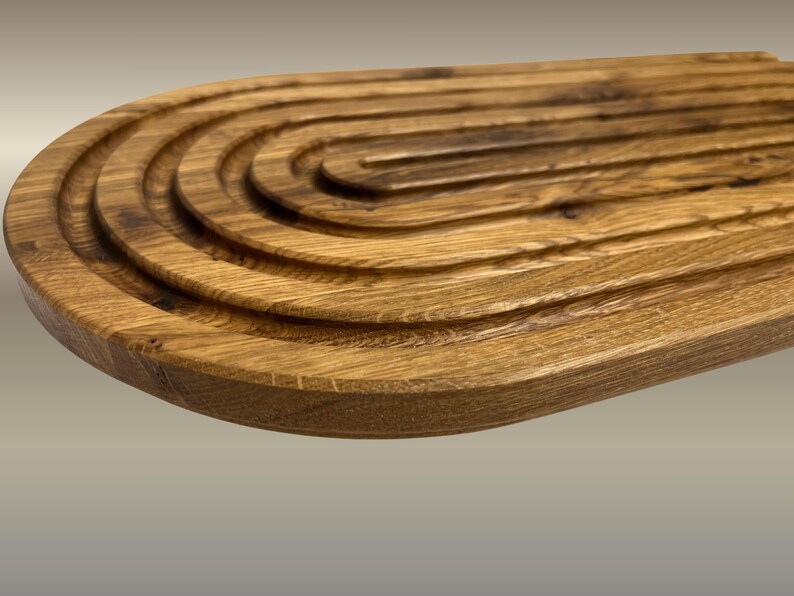 May include: A wooden breadboard with a unique design. The board is made of light brown wood and features a series of concentric, curved grooves. The grooves create a visually appealing texture and are ideal for serving bread or other foods.