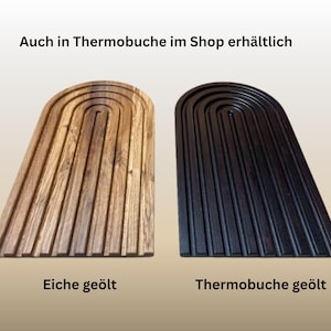 May include: Two wooden serving boards, one light brown and one black, each with a unique arched design and grooved surface. The text at the top says "Auch in Thermobuche im Shop erh&auml;ltlich". The bottom text says "Eiche ge&ouml;lt" and "Thermobuche ge&ouml;lt".