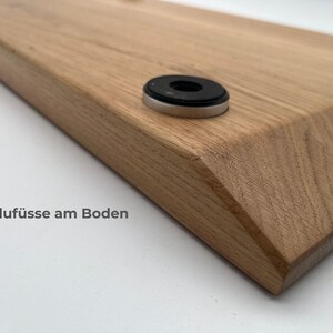 May include: A light brown wooden board with beveled edges featuring circular silver-toned metal feet with black rubber pads attached to the underside. The text Aluf&uuml;sse am Boden is printed on the surface near the corner of the wooden board.