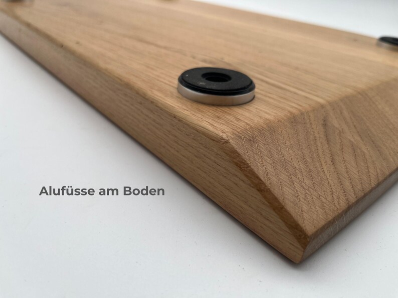 May include: A light brown wooden board with beveled edges featuring circular silver-toned metal feet with black rubber pads attached to the underside. The text Aluf&uuml;sse am Boden is printed on the surface near the corner of the wooden board.