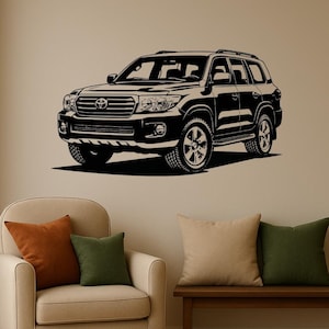 May include: Black and white graphic of a sport utility vehicle (SUV) on a wall. The SUV is a detailed illustration, showcasing its front grille, headlights, and tires. The image is mounted above a beige armchair with orange and green throw pillows.