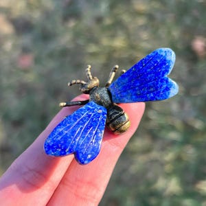 May include: A lapis lazuli bee ornament with brass-coloured metal detailing. The bee features bright blue wings and a body combining blue and brass tones. This is a decorative item.