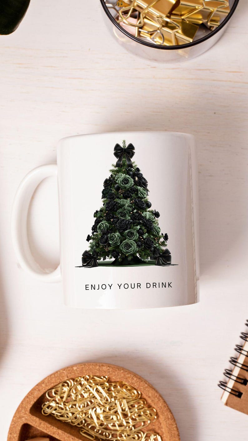 Pode incluir: Caneca de cer&acirc;mica branca com um desenho de &aacute;rvore de Natal feito de rosas pretas e verdes, adornada com la&ccedil;os pretos. A caneca tem uma al&ccedil;a branca e o texto "ENJOY YOUR DRINK". Uma caneca festiva com tema de feriado.