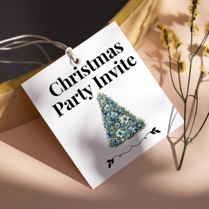 Pode incluir: Etiqueta branca de convite para a festa de Natal com texto preto e um desenho floral de &aacute;rvore de Natal em tons de azul. A etiqueta &eacute; presa com um fio branco.