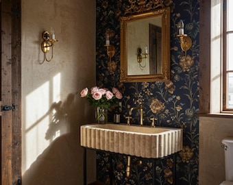 May include: A bathroom interior featuring a stone sink with a ribbed design, gold fixtures, and a black metal stand. The room has floral wallpaper, a gold-framed mirror, and sconces. A vase of pink roses sits on the sink.