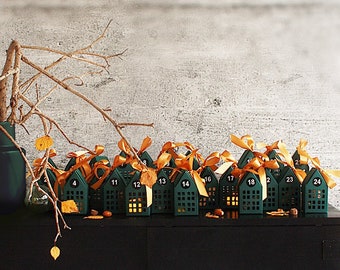 May include: A dark green advent calendar with house-shaped boxes, each numbered and tied with orange ribbons. A dark vase with branches and leaves sits on a black cabinet. The background is a textured gray wall.