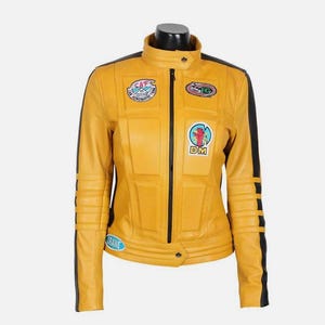 May include: Mustard yellow leather jacket with black stripes and patches. The jacket has a stand-up collar, a front zipper, and multiple patches with text and graphics. The sleeves have ribbed detailing, and the jacket is displayed on a mannequin.