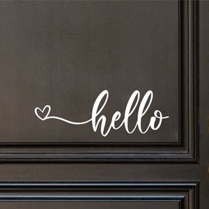 Può includere: Una porta nera con una maniglia dorata e un adesivo in vinile bianco che dice "hello" con un piccolo cuore davanti alla parola.