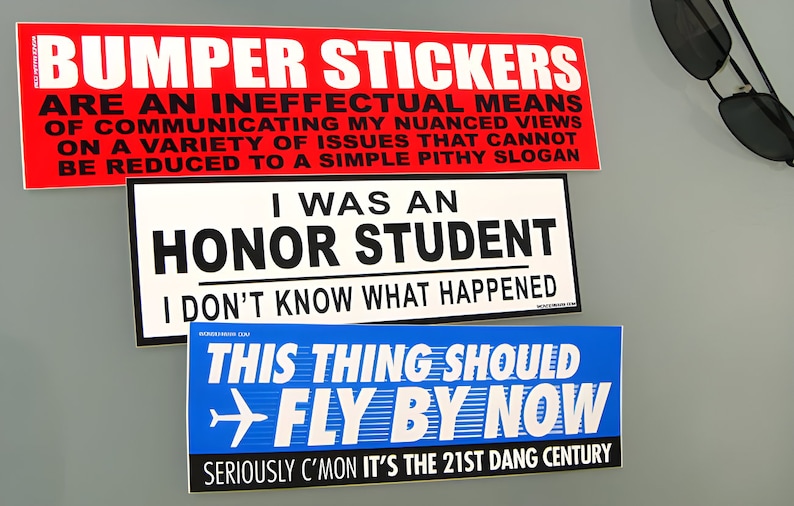 May include: Three rectangular bumper stickers with text. The top is red with white and black text reading BUMPER STICKERS ARE AN INEFFECTUAL MEANS OF COMMUNICATING MY NUANCED VIEWS. The middle is white with black text reading I WAS AN HONOR STUDENT I DON'T KNOW WHAT HAPPENED. The bottom is blue with white text reading THIS THING SHOULD FLY BY NOW SERIOUSLY C'MON IT'S THE 21ST DANG CENTURY.