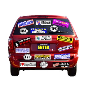 May include: A red SUV rear view covered in various rectangular and oval bumper stickers with text including God Bless America, Ed Zabrocki, I'd Rather Be Fishing, Talk Radio WMMX, Hang Up and Drive, Caution Driver Is Singing, and Honor Student.