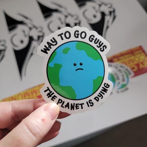 May include: A white sticker with a blue and green cartoon earth with a sad face. The sticker says "Way to go guys the planet is dying."