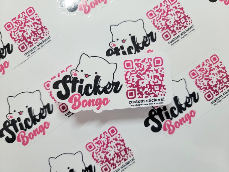 May include: A collection of white stickers with a pink and black design. The stickers feature a cartoon cat with a QR code and the text "Sticker Bongo" in a pink and black font. The text "custom stickers!" is also included on the stickers.