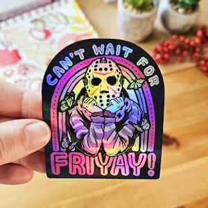 May include: A holographic sticker with a rainbow background and a character wearing a hockey mask. The text on the sticker reads "Can't Wait For Friyay!"