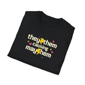 May include: Black t-shirt with a yellow lightning bolt and the text "they/them causing mayhem" in a yellow font with pink hearts and stars.