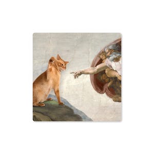 May include: A square print featuring a humorous parody of Michelangelo's 'The Creation of Adam.' An orange cat is depicted in place of Adam, reaching towards God's finger. The background mimics the original fresco's style.