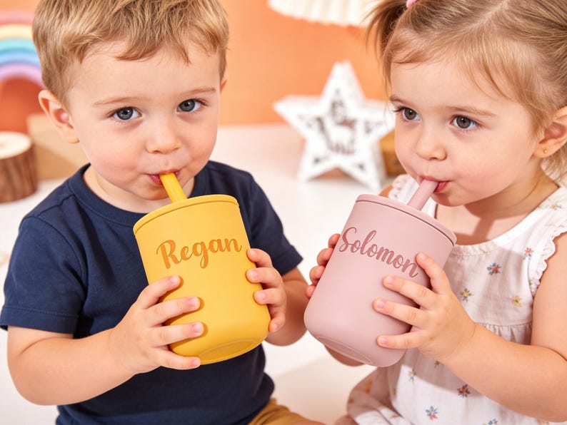 Puede incluir: Dos ni&ntilde;os bebiendo de vasos personalizados. Un vaso es de color amarillo mostaza con el nombre "Regan" impreso, y el otro es de color rosa empolvado con el nombre "Solomon". Ambos vasos tienen pajitas a juego.