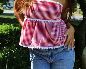 Peut inclure: Haut bustier à carreaux rouges et blancs avec bordure en dentelle blanche. Le haut est associé à un jean bleu. La tenue est portée en extérieur dans un cadre naturel.