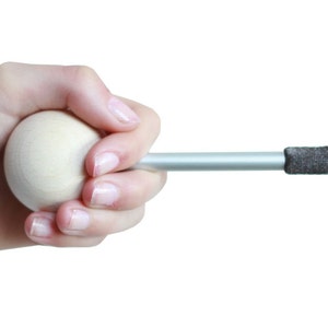 Puede incluir: Una mano sostiene una bola de madera unida a una varilla plateada con una punta de tela gris.