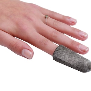 Peut inclure: Un protège-doigt gris en tissu doux et texturé. Le protège-doigt est porté sur l'index d'une main.