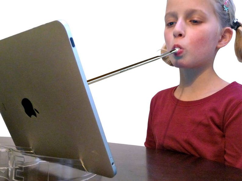 May include: A young person with blonde pigtails uses a long, silver straw to drink from a tablet computer propped up on a clear stand. The tablet is silver and has an Apple logo on the back.