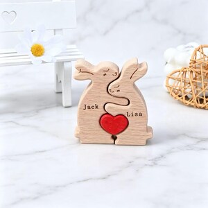 Peut inclure: Deux figurines de lapins en bois clair debout ensemble dans une étreinte. Le lapin de gauche est gravé avec le nom Jack et celui de droite avec le nom Lisa. Un petit cœur en bois rouge vif est placé entre les deux personnages.