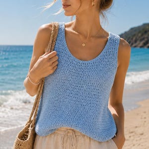 May include: A light blue sleeveless crochet top with a scoop neckline paired with beige drawstring trousers and a tan woven straw tote bag. The top features a textured knit pattern, while the trousers have a relaxed fit and a tied waist detail.