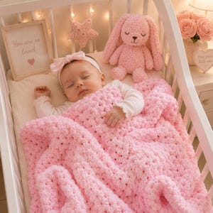 May include: A baby sleeps peacefully in a white crib, covered by a soft, pink, crocheted blanket. A matching pink crocheted bunny and star-shaped decoration are in the crib. A framed sign reads "You are so loved".