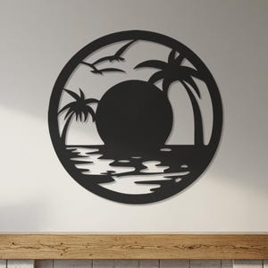 Puede incluir: Arte mural de metal negro que representa una escena de puesta de sol con palmeras, pájaros y agua dentro de un marco circular. La obra de arte está montada en una pared blanca sobre una chimenea con una repisa de madera. La habitación presenta una paleta de colores neutros.