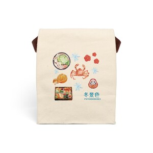 以下が含まれることがあります： 茶色の持ち手が付いたベージュ色のトートバッグ。カニ、オレンジスライス、雪の結晶、花、ダルマ人形の日本のイラストが特徴です。「冬景色 FUYUGESHIKI」の文字がバッグにプリントされています。