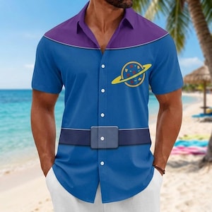 May include: A short-sleeved button-down shirt featuring a blue base with a purple yoke across the shoulders. The shirt displays a yellow planet graphic with colorful spots on the chest and a printed dark blue belt design across the waist area.