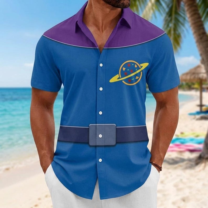 May include: A short-sleeved button-down shirt featuring a blue base with a purple yoke across the shoulders. The shirt displays a yellow planet graphic with colorful spots on the chest and a printed dark blue belt design across the waist area.