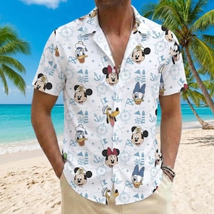 Op de afbeelding: Een wit overhemd met korte mouwen en knoopsluiting, voorzien van een all-over print van Disney-figuren zoals Mickey Mouse, Minnie Mouse, Donald Duck, Daisy Duck en Pluto met zeemansmutsen, afgewisseld met blauwe ankers, kompassen en vlaggen.