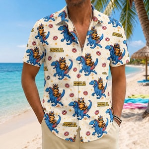 May include: A short-sleeved button-down shirt in cream featuring a repeating pattern of blue dinosaurs with orange cats wearing sunglasses riding on their backs, pink donuts, and the text "MONGO IS APPALLED!" printed in black capital letters.