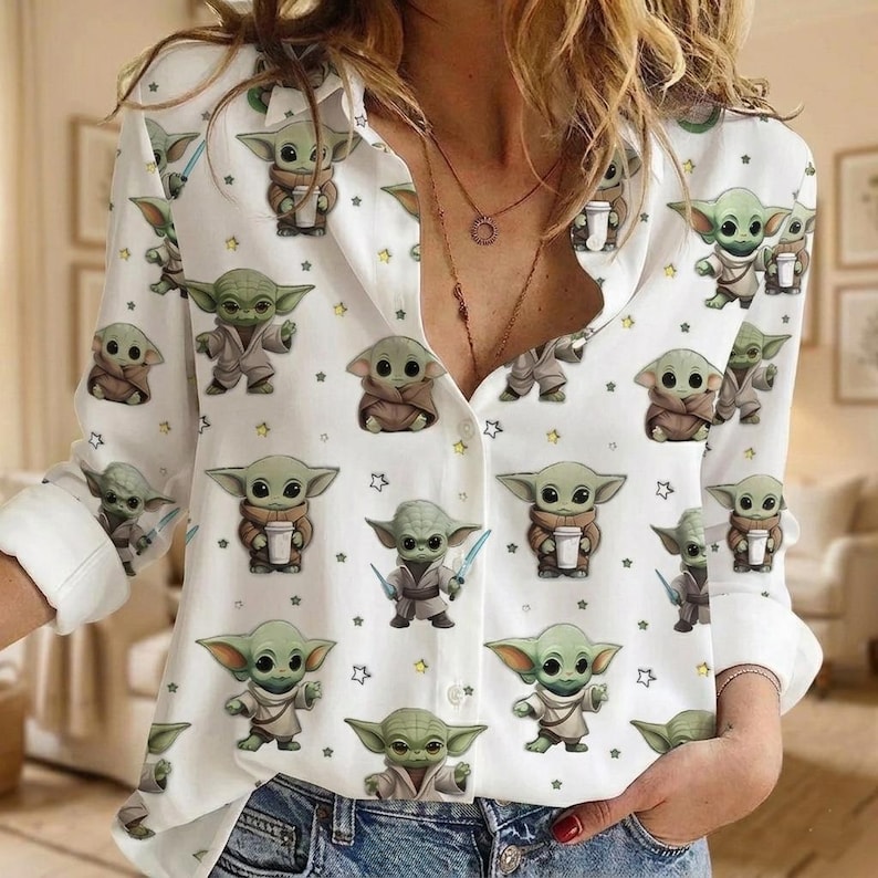 May include: A white long-sleeve button-down shirt featuring an all-over print of small green alien characters in various poses, including some holding cups or lightsabers, interspersed with small yellow stars across the fabric.