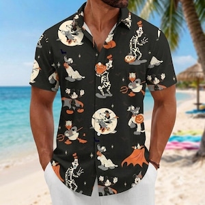 May include: A black short-sleeve button-down shirt featuring an all-over Halloween-themed print of cartoon characters dressed in costumes, including skeletons, vampires, and mummies, accented with orange pumpkins, stars, and bats.