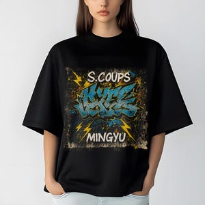 May include: Black t-shirt featuring a graffiti-style design with the words "S.COUPS", "HYBE", and "MINGYU" in blue and yellow. The design has a distressed, vintage look with lightning bolt accents.